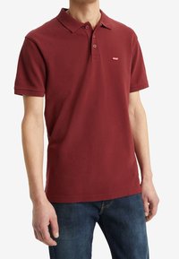 Polo shirt bordeaux en coton, avec un col classique, trois boutons et un petit logo rouge Levi's sur le côté gauche de la poitrine.