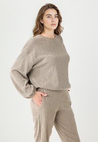 Ensemble de vêtements d'intérieur texturé beige comprenant un pull ample à manches longues et un pantalon tapered assorti avec des poches latérales.