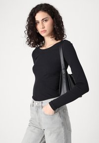Svart ribbet langermet topp paret med lysegrå høyhalsjeans. Modellen holder en svart håndveske som fremhever et enkelt design og teksturer.
