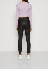 Czarne, dopasowane spodnie wykonane z błyszczącego materiału, w połączeniu z krótką jasnoliliową bluzką z długim rękawem. Białe sneakersy z limonkowymi akcentami.