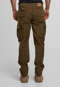 Ruskeat corduroykangashousut, joissa on läppäpocketit ja teksturoitu pinta. Vyötärönauhaan on ommeltu merkki, ja lahkeissa on joustavat resorit.