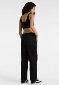 Zwarte cropped tanktop en losse zwarte cargobroek met elastische tailleband, zijzakken en gestructureerde stof; gedragen met zwart-witte sneakers.