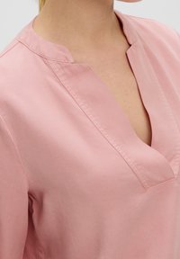Blusa di cotone rosa con scollatura a plissettatura e una texture morbida. Presenta un taglio rilassato e dettagli di cucitura minimi sul colletto.