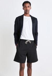 Navy blazer over a white t-shirt, paired with black sweat shorts featuring a drawstring. Modest fit with a casual design.