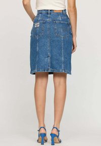 Jupe midi en denim bleu avec une coupe droite, deux poches arrière et des détails de couture. Associée à des sandales à talons hauts bleues.