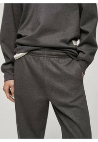Sweatshirt gris et pantalon de survêtement assorti en tissu doux; possède une coupe décontractée, une taille élastique et un détail de doublure intérieure blanche.