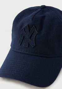 Boné de beisebol em feltro azul-marinho com costura escura em relevo e logótipo bordado. Viseira pré-curvada e tecido texturizado visível.