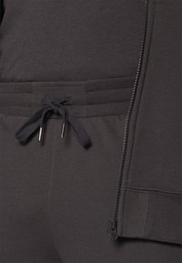 Zwarte ritsjack met een textuurafwerking, voorzien van een verstelbare trekkoord taille en een zijrits zak. Glad materiaal met subtiele details.