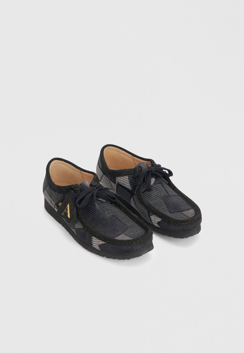 Mocassins en velours côtelé noir et gris à lacets avec une semelle basse, dotés d'une doublure intérieure beige et d'un détail lettre "A" doré sur le côté.