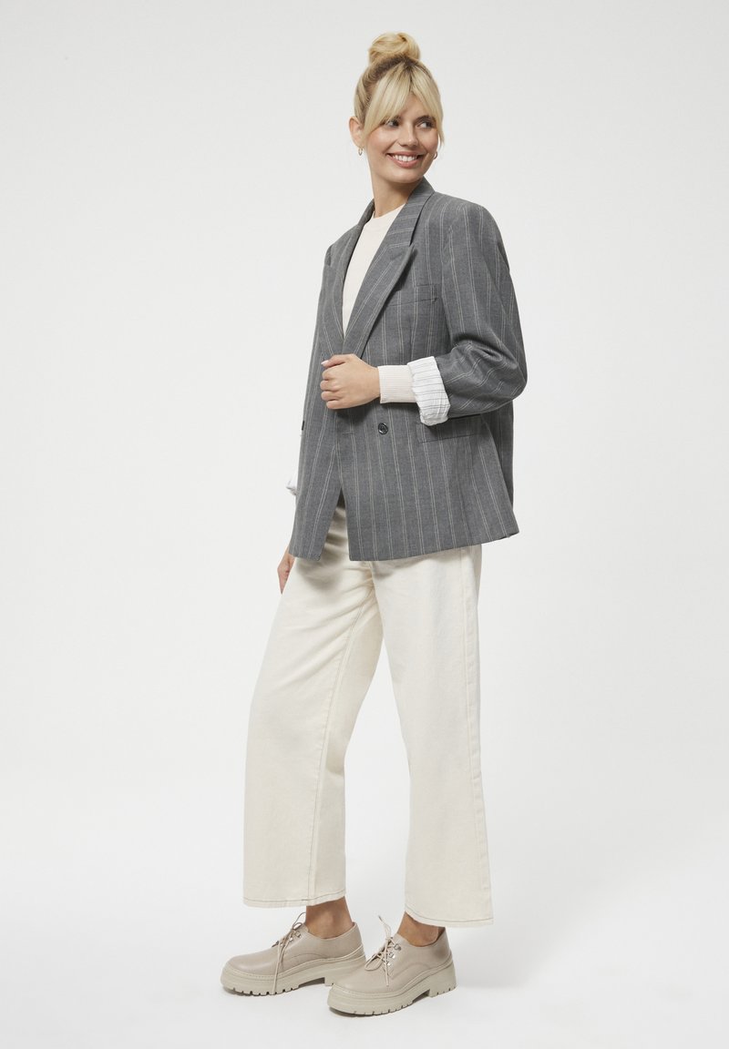 Szary garnitur w prążki, podwójnie zapięty, kremowy sweter, jasnobeżowe spodnie o szerokich nogawkach oraz beżowe platformy na sznurowadłach. Gładkie tekstury i jasne kolory.