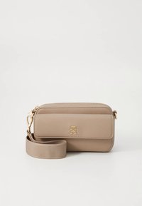 Beežist nahast risti kantav käekott tõmblukuga, millel on kuldne logo, eemaldatav rihm ja sile tekstuur. Kompaktne ja ümmarguse kujuga disain.