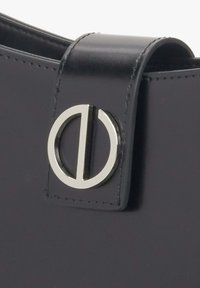 Zbliżenie na czarny skórzany pasek torby z okrągłym metalowym zapięciem w kolorze srebrnym, z pionową belką pośrodku.