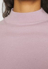 Fialový pletený rolák s přiléhavým střihem a elastickou texturou. Výstřih je vysoký a látka vypadá měkce.