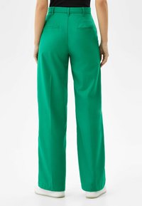 Gröna vida byxor med en slät textur, med bakfickor, en åtsittande midja och minimal hårdvara. Styla med vita sneakers.