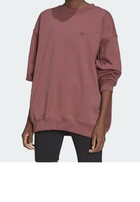Person som bär en överdimensionerad mauve sweatshirt med en liten logotyp på vänster bröst och svarta ribbade cykelshorts.