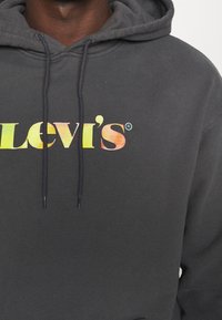 Felpa grigia scura con cappuccio e cordino, con un logo colorato "Levi's" sul petto. Tessuto morbido e design casual.