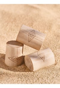 Tres bloques cilíndricos de madera clara con logotipos en forma de diamante descansan sobre arena fina.