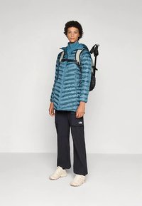 Roheline isoleeritud jope horisontaalse tikandiga, kõrge krae ja tõmblukuga. Kandis tumedaid pükse ja beeže tenniseid, kaasas must seljakott.