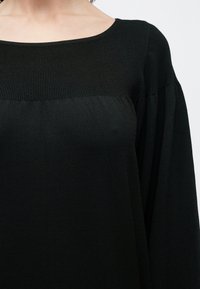 Μαύρο μπλουζάκι με στρογγυλή λαιμόκοψη και ριμπυ υφή στους ώμους. Το ύφασμα είναι απαλό, με άνετη εφαρμογή και πιεσμένα μανίκια.