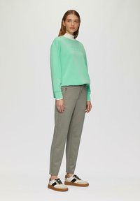 Miętowy sweter z teksturowanym napisem, zestawiony z wzorzystymi szarymi spodniami oraz beżowymi sneakersami z czarnymi akcentami. Prosty, nowoczesny design.