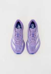 Zapatillas deportivas moradas con parte superior de malla, sistema de cordones y detalles en blanco. Cuenta con una superficie texturizada y una plantilla azul.