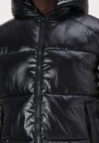 Jachetă tip puffer neagră cu un finisaj lucios, având guler înalt, închidere cu fermoar complet și buzunare laterale. Designul include secțiuni matlasate.