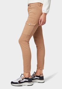 Pantalones cargo slim-fit color marrón claro con bolsillos laterales, a la altura del tobillo y con una textura suave, combinados con zapatillas deportivas en blanco y negro.