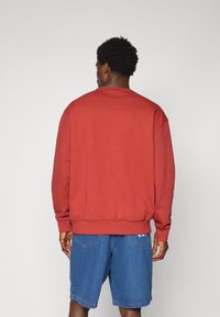 Sweat-shirt en coton rouge avec un col rond et des manches longues, doté de poignets et d'un ourlet côtelés, associé à un short en denim bleu.