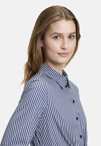 Camicia a righe blu navy e bianca, con colletto, maniche lunghe e bottoni neri. Texture morbida e silhouette aderente.