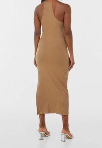 Robe midi en tissu côtelé de couleur beige avec un design à col halter. Le tissu a une texture lisse, complété par des sandales à talons transparents.