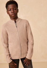 Cárdigan beige de punto acanalado con cuello alto y cremallera completa, con mangas largas y detalles sutiles de textura.