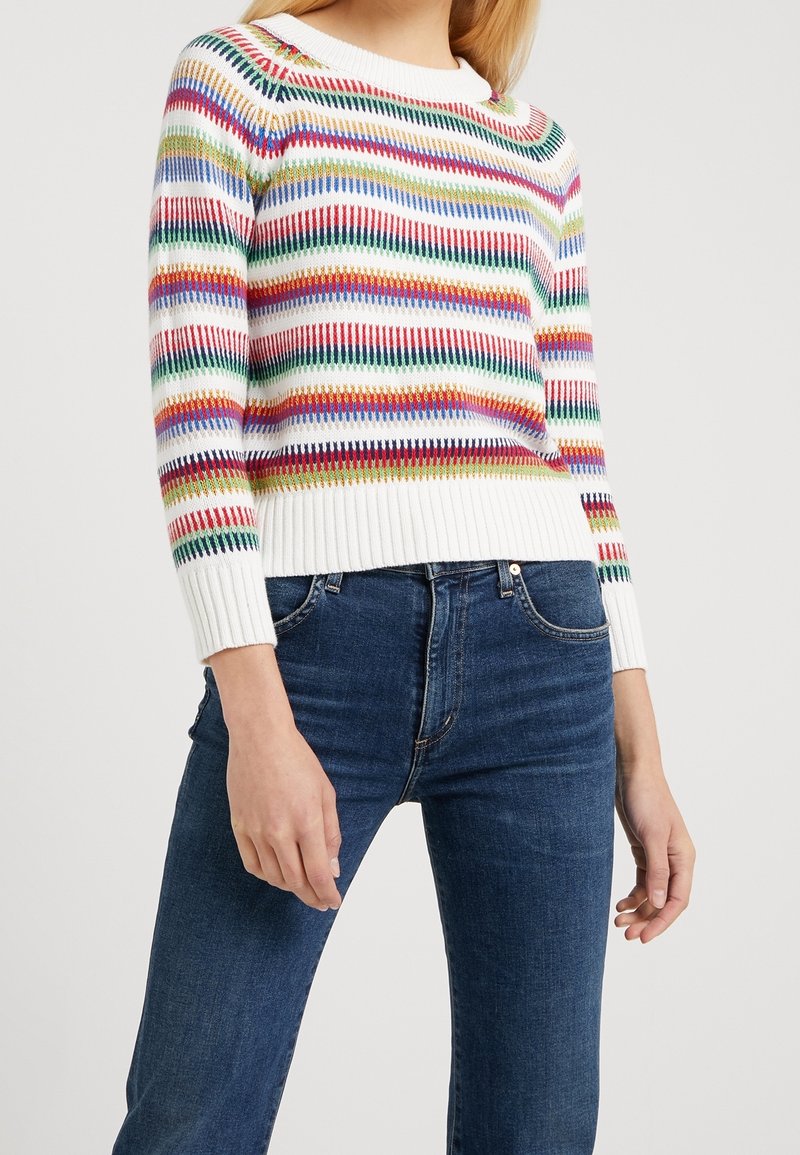 Suéter de punto a rayas en blanco con rayas horizontales coloridas; puños y dobladillo acanalados; combinado con jeans azul oscuro. Corte y textura casual.