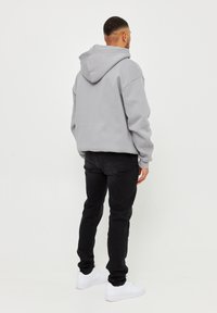 Felpa grigia con cappuccio e spalle cadute, abbinata a jeans neri e sneakers bianche. Il tessuto appare morbido con una vestibilità comoda.