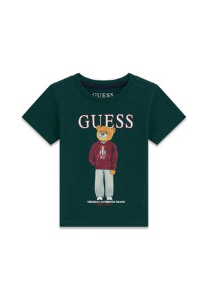 Ciemnozielona koszulka z krótkim rękawem z ilustracją niedźwiedzia ubranej w bluzę z kapturem i spodnie oraz słowem „GUESS” nad nią.