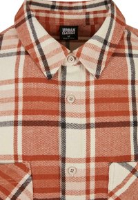 Kostkovaná flanelová košile v oranžové, bílé a černé barvě s špičatým límcem, dvěma knoflíky a přední kapsou. Štítek uvádí "Urban Classics".
