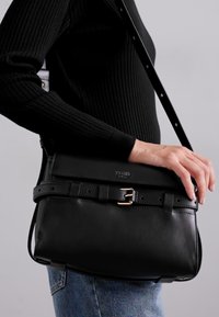 Bolsa de mão em couro preto com forma estruturada, alça destacável, ferragens em tom de ouro e uma aba texturizada com detalhe de fivela.