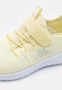 Jasnożółte dziane sneakersy z białą podeszwą, z logo Kappa z boku, elastycznymi sznurówkami oraz rzepem na górze.