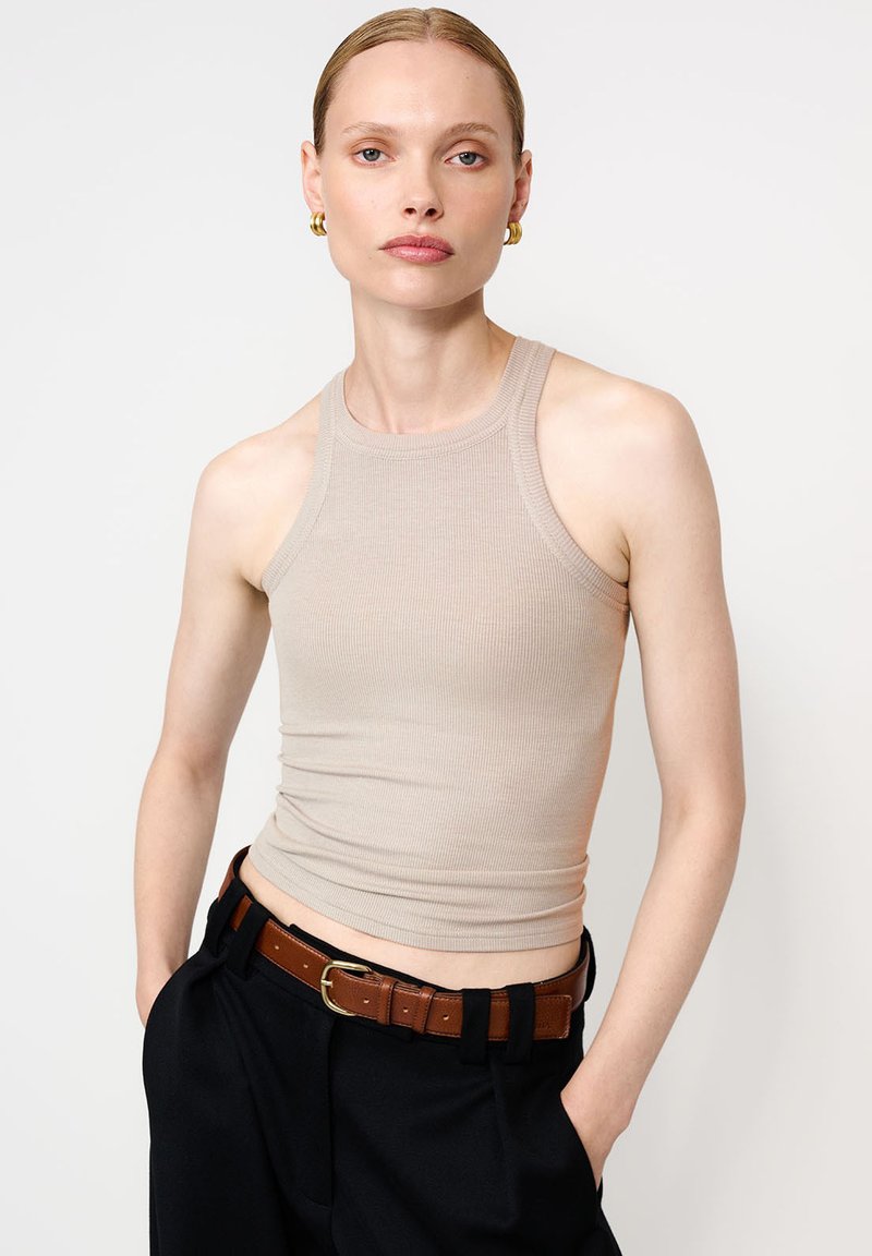 Beige ribaga tank top, mille sobiva disainiga ja võistlus tagasi lõikega. Kombineeritud kõrge vöökohaga mustade pükstega ja pruuni vööga.