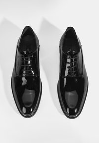 Schwarze Lackleder-Schnürschuhe mit glatter Oberfläche, runder Spitze und strukturiertem Schnürdesign. Minimalistisch mit dezenten Steppnähten.