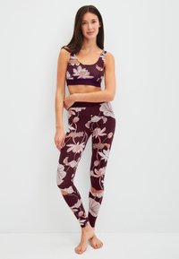 Sportbeha en legging set in donker bordeaux met een bloemenpatroon in lichtroze en crème. Zachte, rekbare stof. Geen zichtbare hardware.