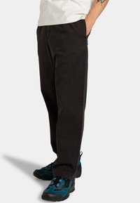Black denim pants with a relaxed fit, sturdy fabric, and side pockets. Worn with textured black and teal athletic shoes.