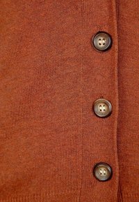 Rdzawoczerwony sweter z dzianiny z czterema okrągłymi guzikami. Tekstura jest gładka, charakteryzuje się ścisłym wzorem dzianiny i ma prosty, casualowy design.