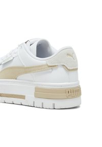 Zapatilla de cuero blanca con un acento de ante beige y una suela media texturizada. Branding notable en el talón y diseño de suela gruesa.