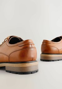 Chaussures en cuir marron avec une texture lisse, bout rond et semelle empilée avec une base en caoutchouc noir et des accents en bois clair.