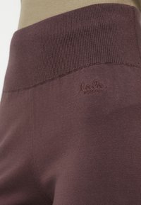 Gros plan sur un pantalon en tricot mauve avec une taille large à côtes et un logo brodé subtil "laLa Berlin" sur la hanche.