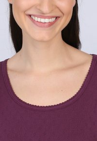 Lila Oberteil mit rundem Halsausschnitt und gewelltem Saum, ausgestattet mit einem strukturierten Muster aus kleinen, erhabenen Punkten. Glattes Material mit einer weichen Oberfläche.