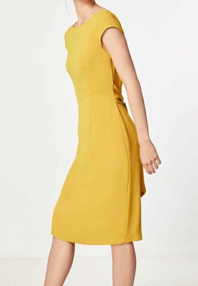 Femme portant une robe jaune moutarde à manches courtes, longueur genou, debout devant un fond blanc uni.