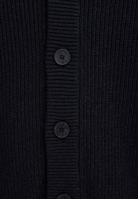 Primo piano di tessuto a maglia costellata scuro con tre bottoni neri impressi con il testo "Polo Club" in allineamento verticale.