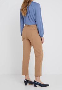 Pantalons beiges au design ajusté, dotés de poches arrière, associés à un chemisier bleu à manches longues et des escarpins en cuir verni marine.