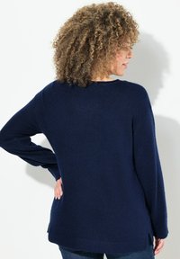 Mörkblå, stickad tröja med långa ärmar, rundad hals, sidofickor och lös passform. Mjuk textur och avslappnad design.